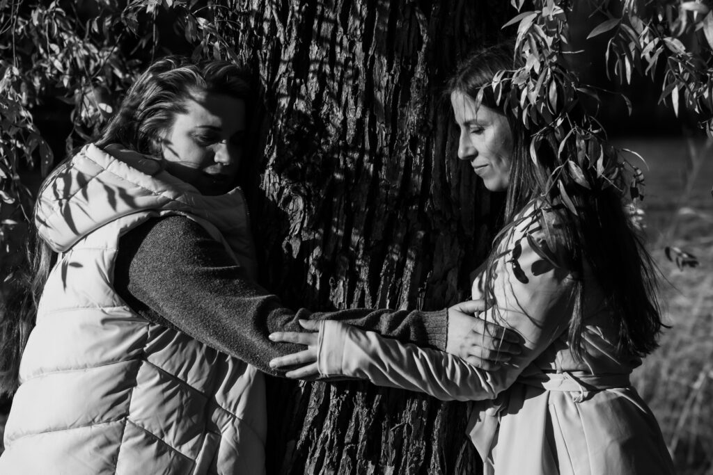 Kuvassa kaksi sairaanhoitajaa saavat turvaa ja halaavat yhdessä puuta.